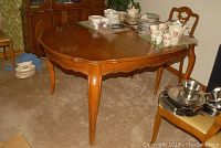 Walnut finish wood dining table in traditional style with scalloped edges and curved legs. Various dinnerware pieces on top but not included.