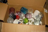 Photo of an open cardboard box filled with assorted drinking glasses, plastic cups, and mugs.