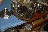 Photo showing a variety of vintage metal dishware items including plates, bowls, and serving platters arranged on a table with a blue cloth.