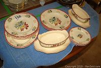 Wide view of all dishes placed on table with blue cloth including 3 side plates, 4 plates, 4 bowls and 2 gravy bowls