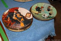 Stack of Norman Rockwell collector plates showing painted family scenes including a couple on a couch and children interacting with a dog.