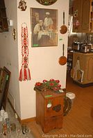 View of the wooden keeper box with metal accents, metal flower wall art placed on top, and the framed Cream of Wheat print hanging on the adjacent wall.
