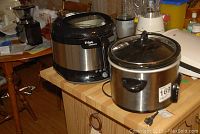 Two kitchen appliances on a wooden table: a T-Fal deep fryer and a Crock Pot slow cooker
