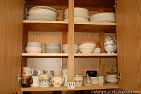 Full view of three wooden shelves filled with assorted kitchenware items including stacks of plates, bowls, and mugs.
