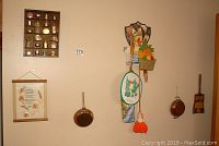 Wall display of wooden compartment shelf holding miniature metal and copper pots, and wall hangings including copper pans and a decorative wooden fruit basket art.