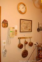Photo of wall hanging items showing copper pans on wooden rack, clock, needlepoint wall art, and wall phone