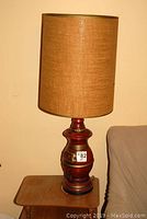 Photo of one chalkware table lamp with reddish finish and burlap cylindrical shade.
