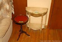Two side tables: a painted wood Demi Lune table with central drawer and bottom shelf, alongside a wooden pedestal table with red leather top in a tripod base.