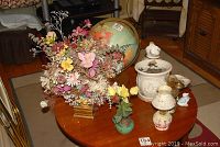 Wide shot showing all lot items on wooden table including globe, faux flowers, oil lamps, ceramic pitcher and planter, and ashtrays.