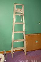 Front view of the 6 ft aluminum step ladder standing against a green wall, showing the steps and top platform.