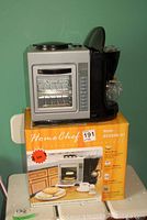 Photo showing Home Chef 3-in-1 breakfast appliance on its original box with clear view of the appliance including mini oven window, coffeemaker side, and egg cooker top.