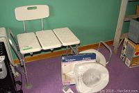 White plastic shower bench with 3-segment seat and backrest next to boxes, on purple carpet