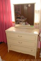Front view of painted wood dresser with mirror on top, showing three drawers with metal pulls and wear marks on the surface.