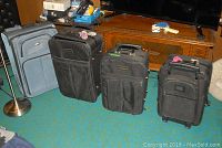 Set of four soft shell suitcases on carpet near wooden cabinet and lamp.