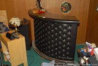 Front and angled view of black tufted vinyl bar counter with faux wood top and wood footrest on bottom.