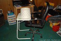 Black faux leather swivel office chair next to white TV food tray table with paper lamp shade placed on top, showing the full lot in a room environment.