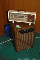 Photo showing the Mastercraft dehumidifier with a brown slanted grille and control panel, topped by the Tastic heater fan with protective mesh and rotary knob.