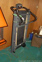 Photo of the Tek Athletic treadmill in folded upright position showing the front and display panel.