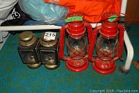 Four portable oil lamps on floor: two red hurricane-style and two black and brass lantern-style lamps