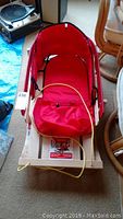 Full view of wooden sled with red nylon padded seat and yellow pull rope attached to front.