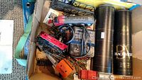 Box containing train set components including transformer, tools, some train cars, and other accessories packed together.