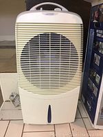 Photo of white Conair Climate Wizard humidifier unit with front fan grille, handle on top, power cord coiled on floor beside it.