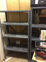Front view of one metal shelving unit with four shelves, dark gray steel, showing adjustable peg holes and surface wear