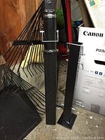 Two black square steel posts—primary vertical hitch post and smaller extension post—leaning against wall