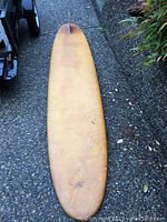 Full top view of vintage longboard surfboard with yellowed surface and visible wear.