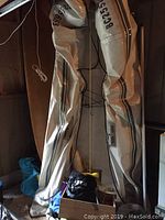 Deflated Zodiac inflatable boat folded upright in shed with wooden oar, black storage bag, braided white rope