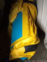Folded blue and yellow inflatable boat with rust marks and some damage on the exterior surface