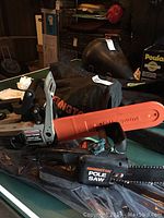 Remington pole saw laying on a flat surface with a visible Craftsman chainsaw handle behind it.