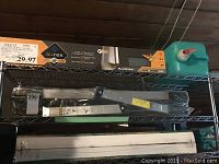 Metal shelving containing Alurex gutter guard in original box, black folding ladder, white plastic items, and a green jug.