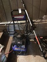 Overall front view showing Simoniz 2350 frame, Briggs & Stratton engine, coiled high-pressure hose and spray wand