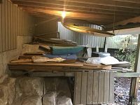 Wide view of stack of cedar siding boards with some rolled foam and wooden structures in basement