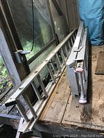 Both aluminum ladders seen from an angle, showing their relative sizes and details such as rubber stabilizing feet and locking mechanisms.