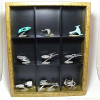 Eleven Star Trek miniature ships displayed on metallic stands inside a gold shadow box with black interior and sliding Plexiglass cover. Ships are arranged in 3 rows of 3 compartments, three ships on bottom row with two together in one compartment.