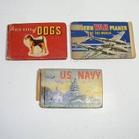 Three vintage pocket books with worn covers: red book featuring a dog, blue book featuring warplanes, and blueish cover book featuring U.S. Navy battleship.