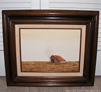 Full view of framed barn painting, showing the rustic barn with a reddish roof in a barren field and wide dark wooden frame.