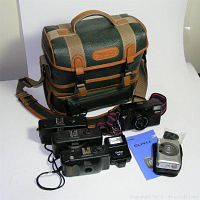 Shows vintage Ambico pebbled faux leather camera bag along with four 35mm black cameras, Canon Elph digital camera, Vivitar flash, and Canon Elph manual.