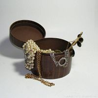 Jewelry pieces spilling out of the open round brown faux alligator textured case showing pearl beads, chains, and earrings