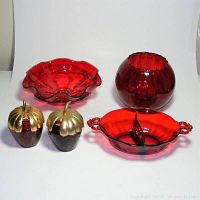 All five red glass serving pieces displayed against a white background: a ruffled bowl, oval divided bowl with handles, round ribbed bowl, two strawberry-shaped jam jars with gold lids, one missing spoon.