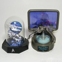 Wide shot showing both Star Trek display models: USS Enterprise in glass dome with asteroid belt and Klingon Bird of Prey model on display with view screen.