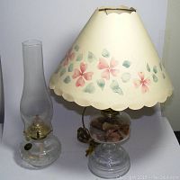 Two glass oil lamps side by side: hobnail pattern lamp with chimney and wick on left, electrified oil lamp with floral lampshade on right