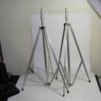 Two metal tripods with screw heads, one tripod slightly extended in height, shown against plain background with computer keyboard nearby for scale