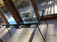 Glass top coffee table with wrought iron frame beside window showing decorative wrought iron detail and glass surface
