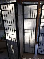 Photo of one tri-fold sun screen/window shade showing black frame and white translucent Shoji grid panels.
