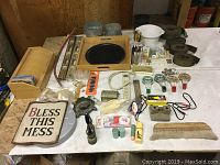 Full view of mixed household items on a table including trays, scales, decorative sign, bottles, and brushes.