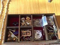 Jewelry box compartments containing small items including cufflinks, ring, star brooch, tie clips, and metal bangles.