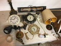 Collection of assorted lamps, clocks, clip-on lights, bulbs on table.